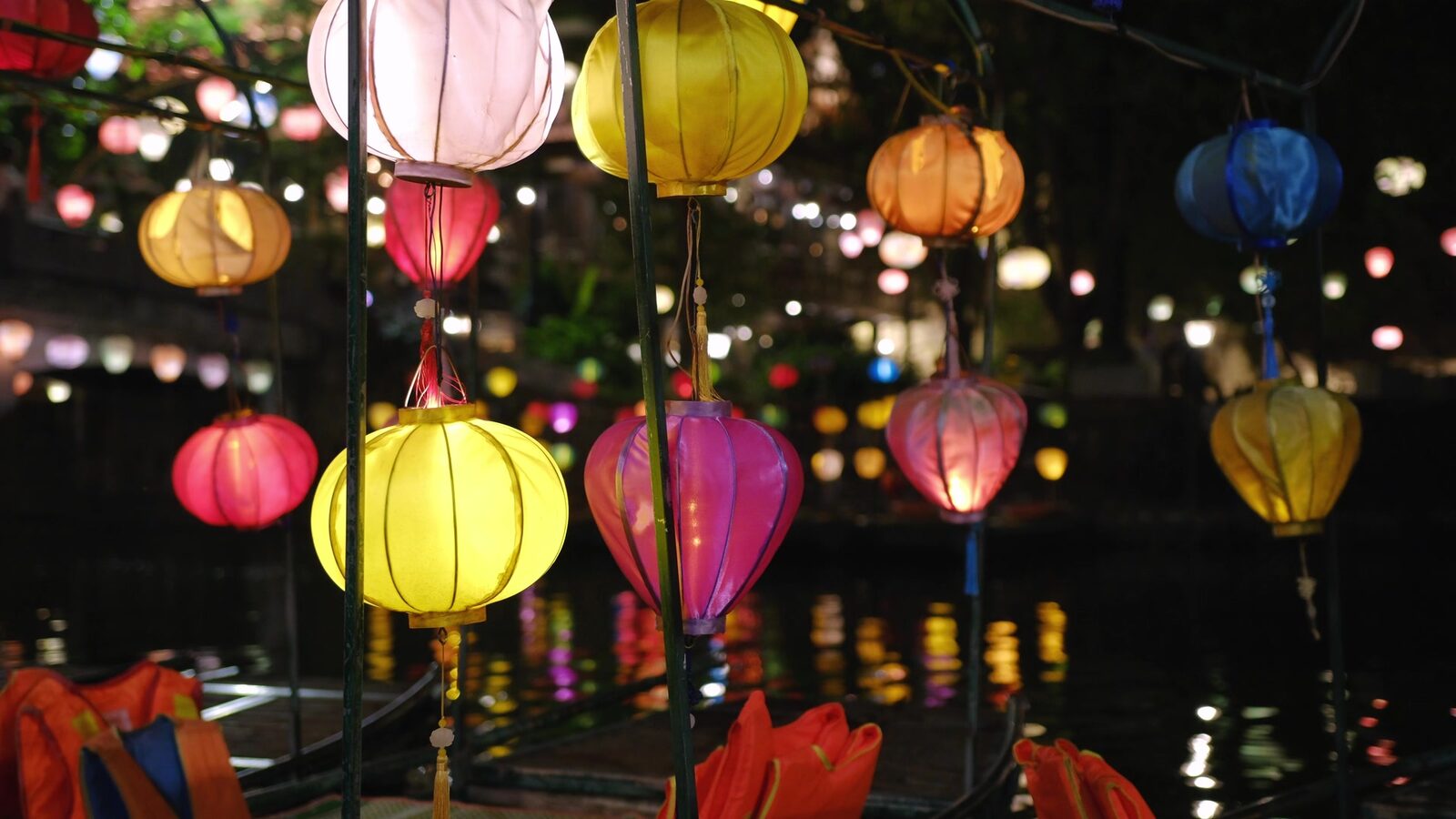 Colourful silk lanterns glowing and reflected on the river at night in Hội An.