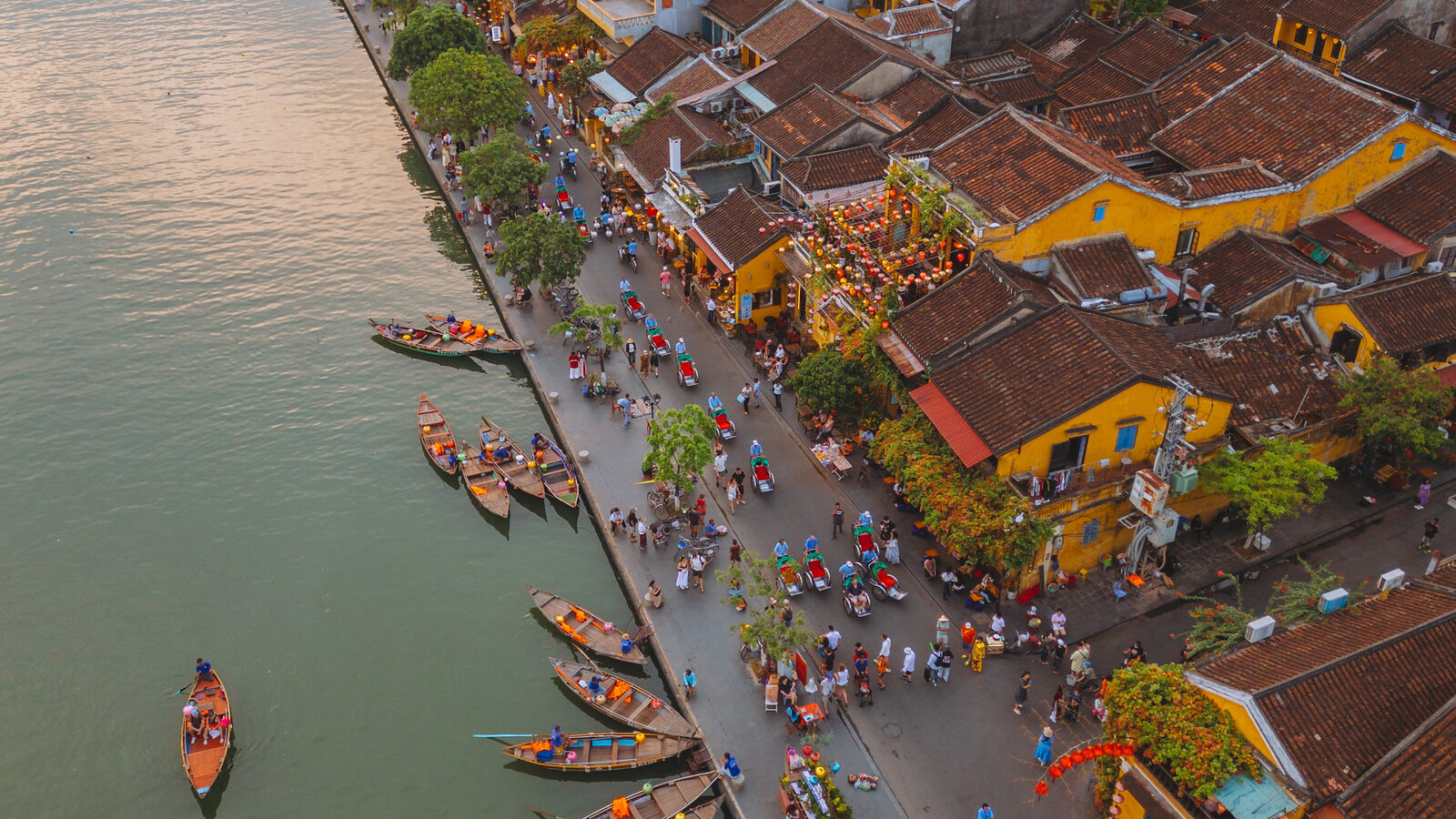 Late-afternoon aerial of the Hội An Ancient Town waterfront, wooden boats moored along the Thu Bồn river.